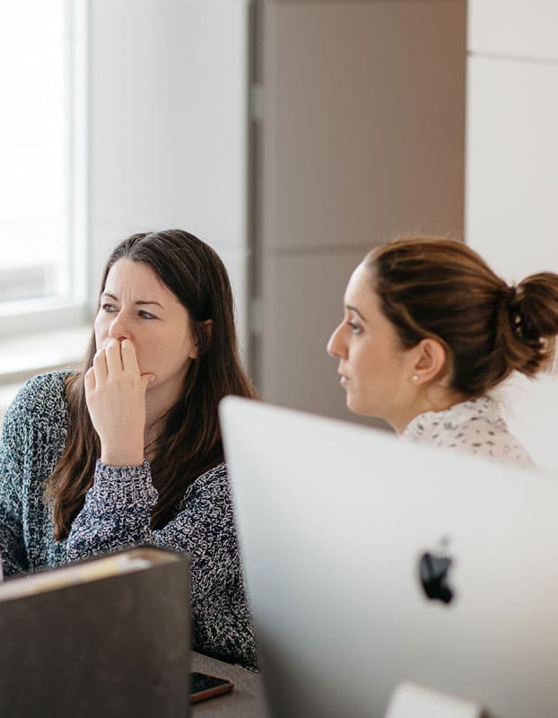 Zwei Kolleginnen verfolgen konzentriert eine Abstimmung am Bildschirm